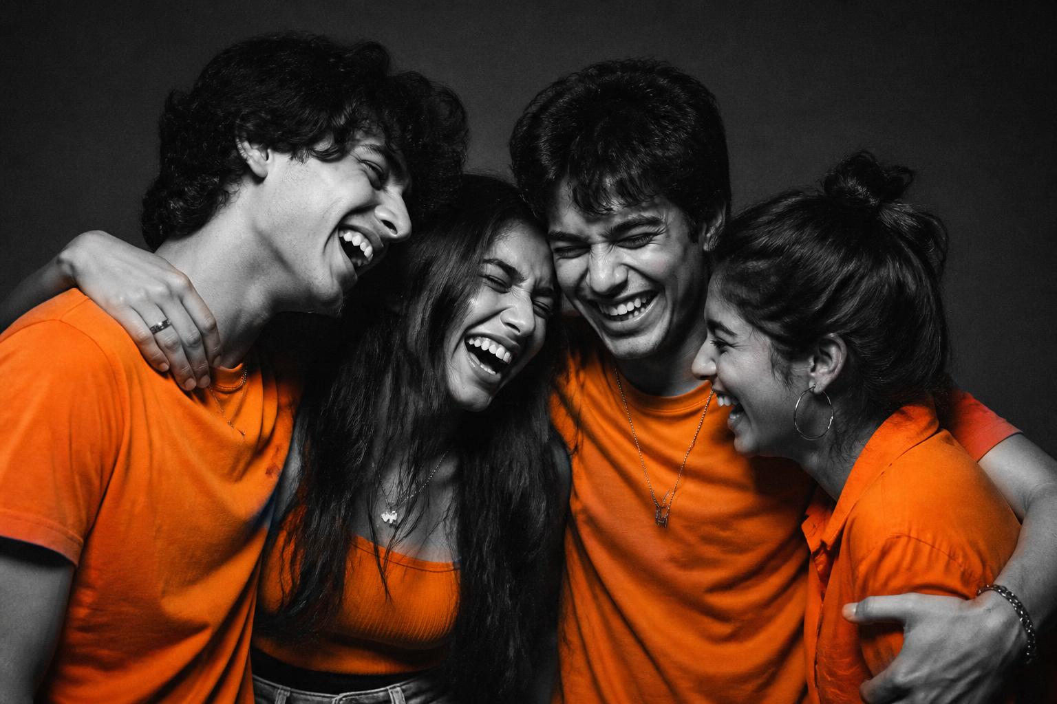 Four Gen Z friends in orange tees laughing together in a huddle